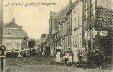De Markt met aan het eind van de Koestraat de nieuwe gemeenteschool. Geheel rechts de winkel van Jacob Crucq. Met in de deuropening mevrouw Crucq-Kwekkeboom. De Markt met aan het eind van de Koestraat de nieuwe gemeenteschool. Geheel rechts de winkel van Jacob Crucq. Met in de deuropening mevrouw Crucq-Kwekkeboom.